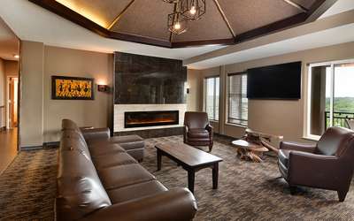 an overview of inside the Penthouse Suite's living room with tv, couch, chair, and large fireplace.