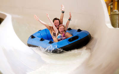 A mom and daughter with their arms up on a water slide