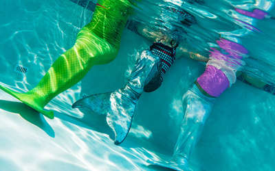 three girls wearing mermaid tails in a pool