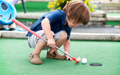 Little boy playing with golf ball and club at minigolf.
