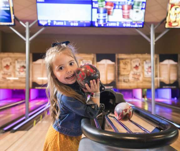 Little girl smiling at camera while holding a bowling ball.