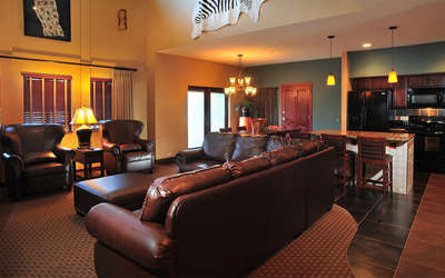 Nyumba Villa living room with a large leather couch and two chairs with a large kitchen in the background