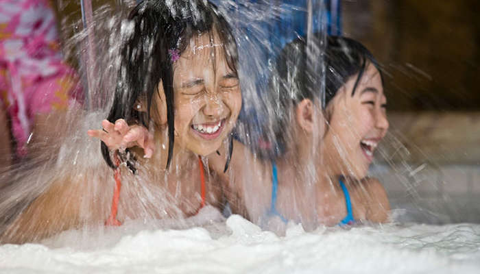 two girls sitting under a small waterfall