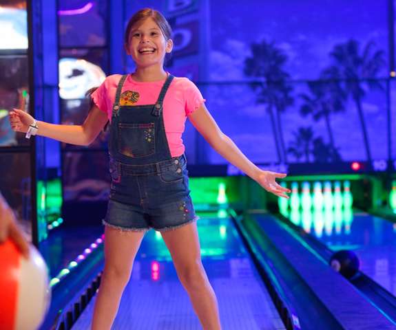 A happy little girl bowling.