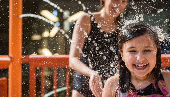 Little girl laughing and getting splashed in the face with water.